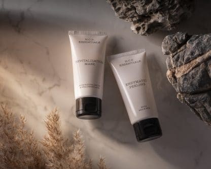 Vegan & fragrance free skincare from N.C.P. Glowing kit with Revitalization Mask a white bottle with black text and black cap & Enzymatic Peeling a white bottle with black text and black cap. Products laying down on a marble background. Stone and dry grass.