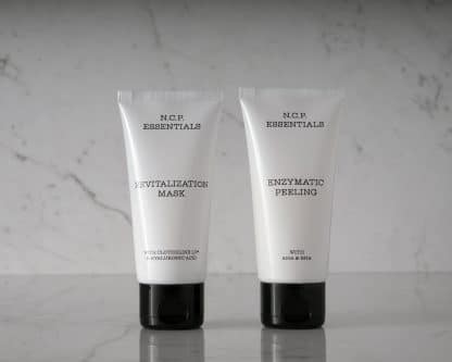 Vegan & fragrance free skincare from N.C.P. Glowing kit with Revitalization Mask a white bottle with black text and black cap & Enzymatic Peeling a white bottle with black text and black cap. Picture is black and white with marble background.