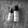 Vegan & fragrance free skincare from N.C.P. Hydration kit with 24 H Face Cream a white bottle with black text and black cap & Hydro Active Serum a white bottle with black text and black pipette.. Products put down in water. Picture is black and white